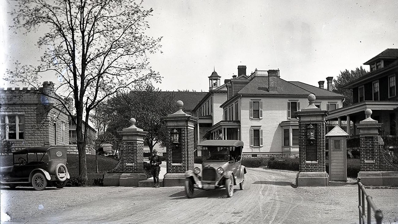 Vintage cars driving past a brick gatehouse.