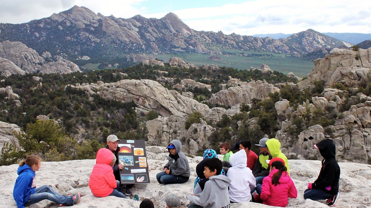 A group of children sit on a rock while listening to a Ranger presentation.