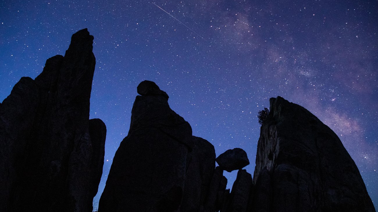A boulder balances among towering granite formations with the milky way overhead.