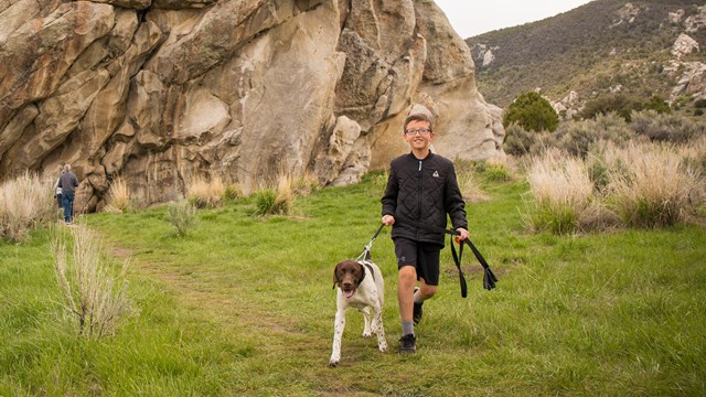 A boy with a dog on a leash hikes through the City of Rocks