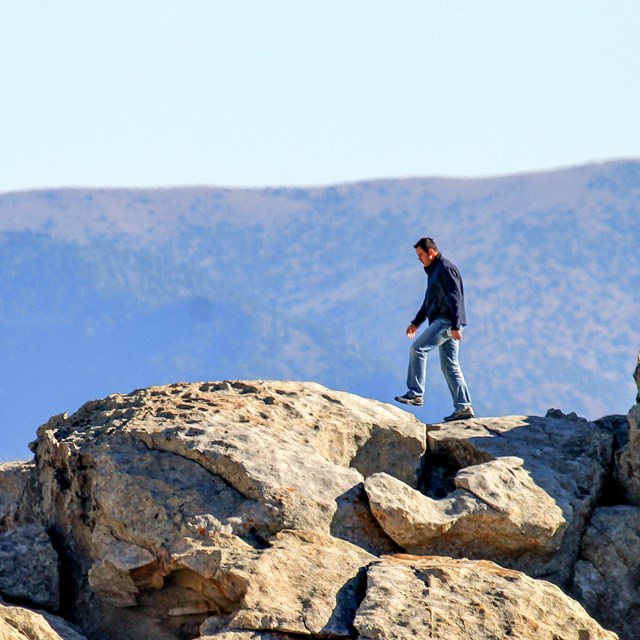 A man walks along the ridge of a granite formations, mountains in the distance.