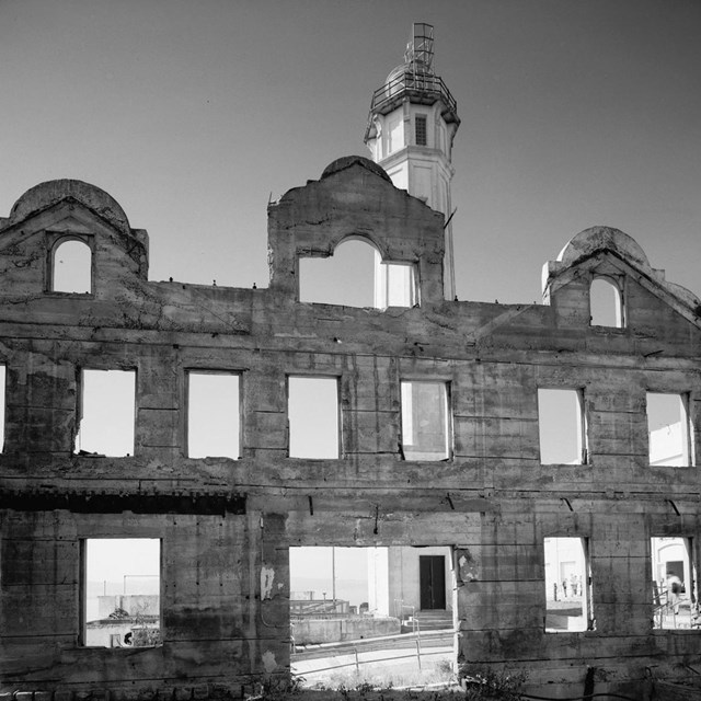 B&W; ruins of brick building with steeple in background