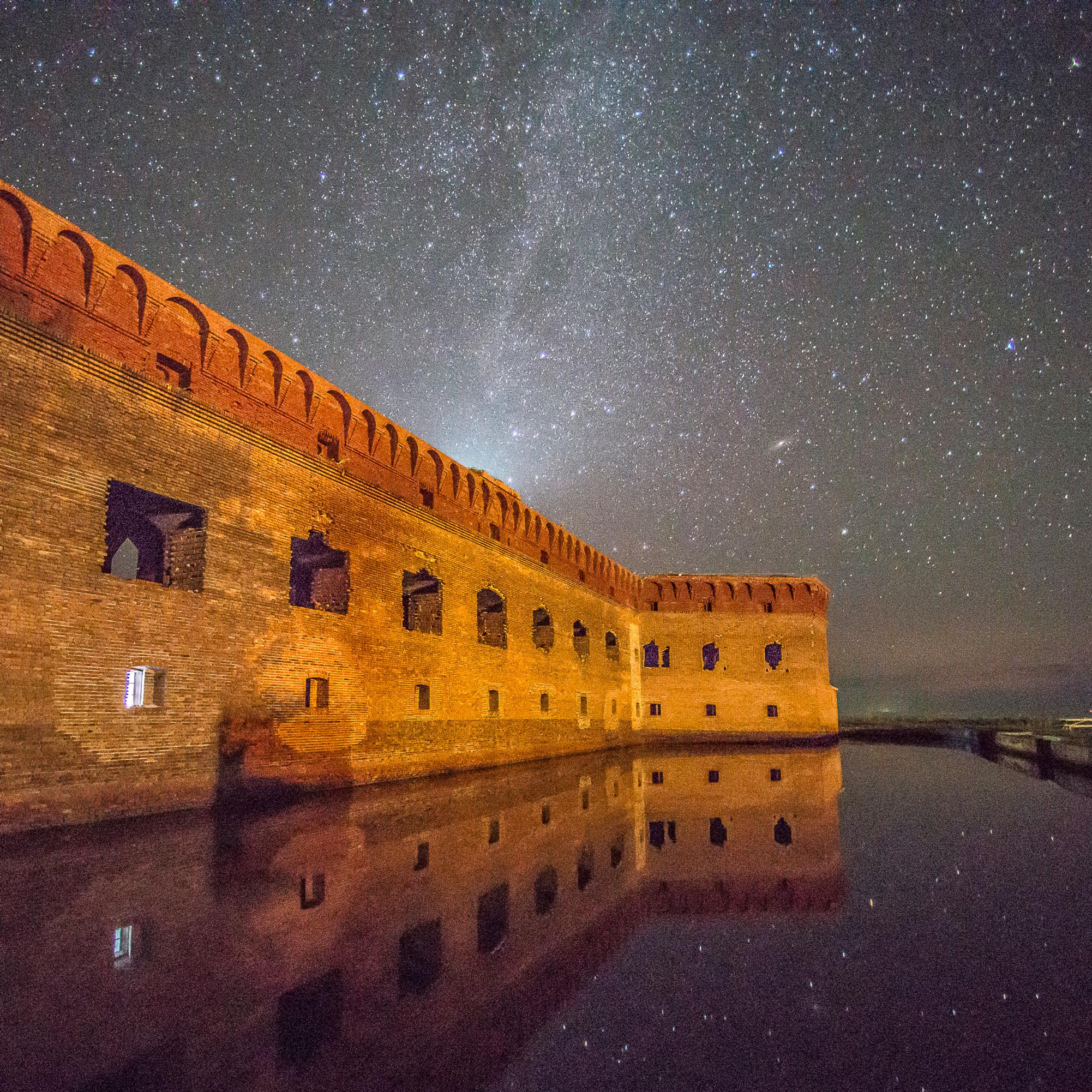 A night view of historic stone fort; thousands of stars shine above and still water reflects it all
