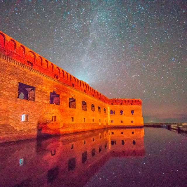 A night view of historic stone fort; thousands of stars shine above and still water reflects it all