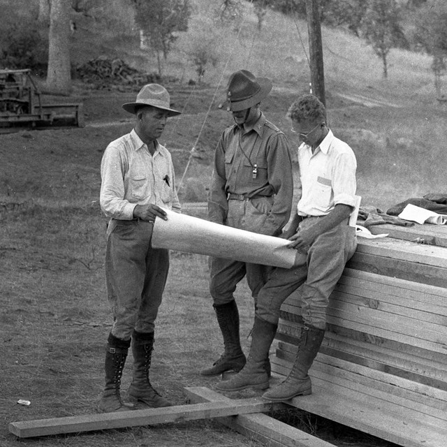 Three men look at a paper together in the 1930s