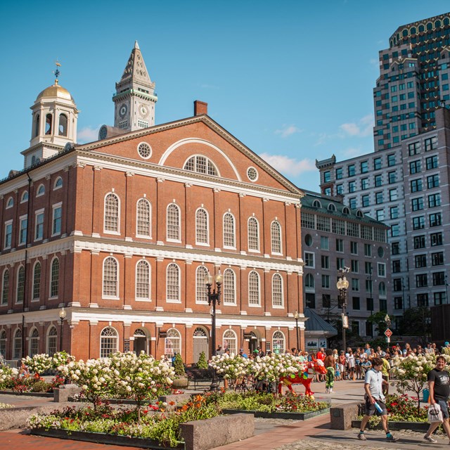 A brick building with white trim in an urban setting, with people in the courtyard in front