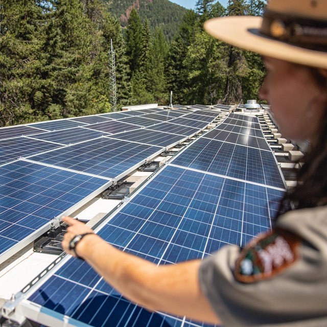 A NPS ranger points at an array of solar panels.