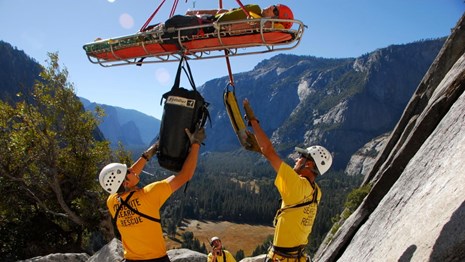 Search and Rescue crew coordinates with helicopter lifting patient from rock face