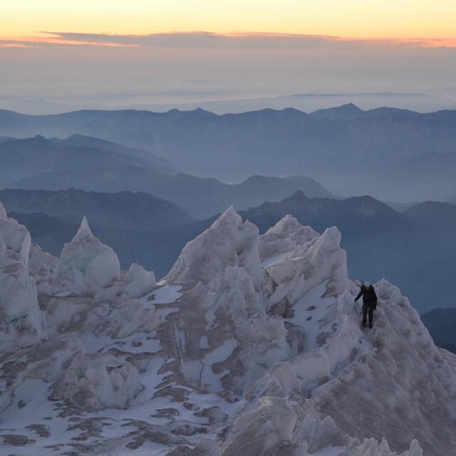 solo figure traversing through glacier seracs, the sun is setting