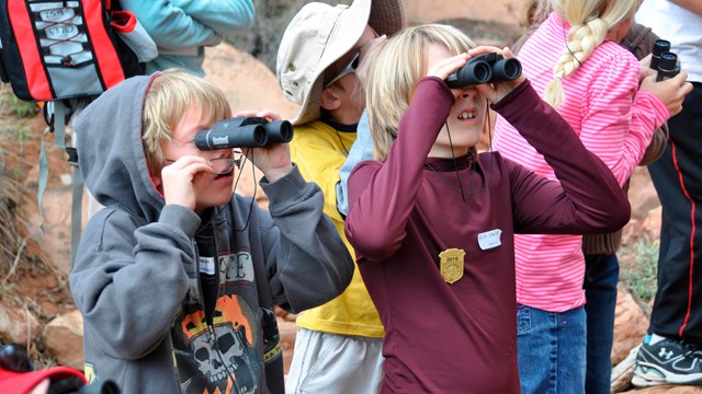 several children hold binoculars to their eyes outdoors