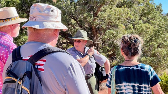 uniformed ranger smiles at three visitors on a hiking trail