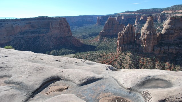 Rock with circular indentions at cliff edge, canyon with red rock monoliths in background 