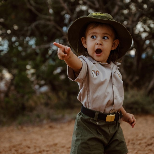 Toddler in Junior Ranger outfit pointing with an expression of amazement.