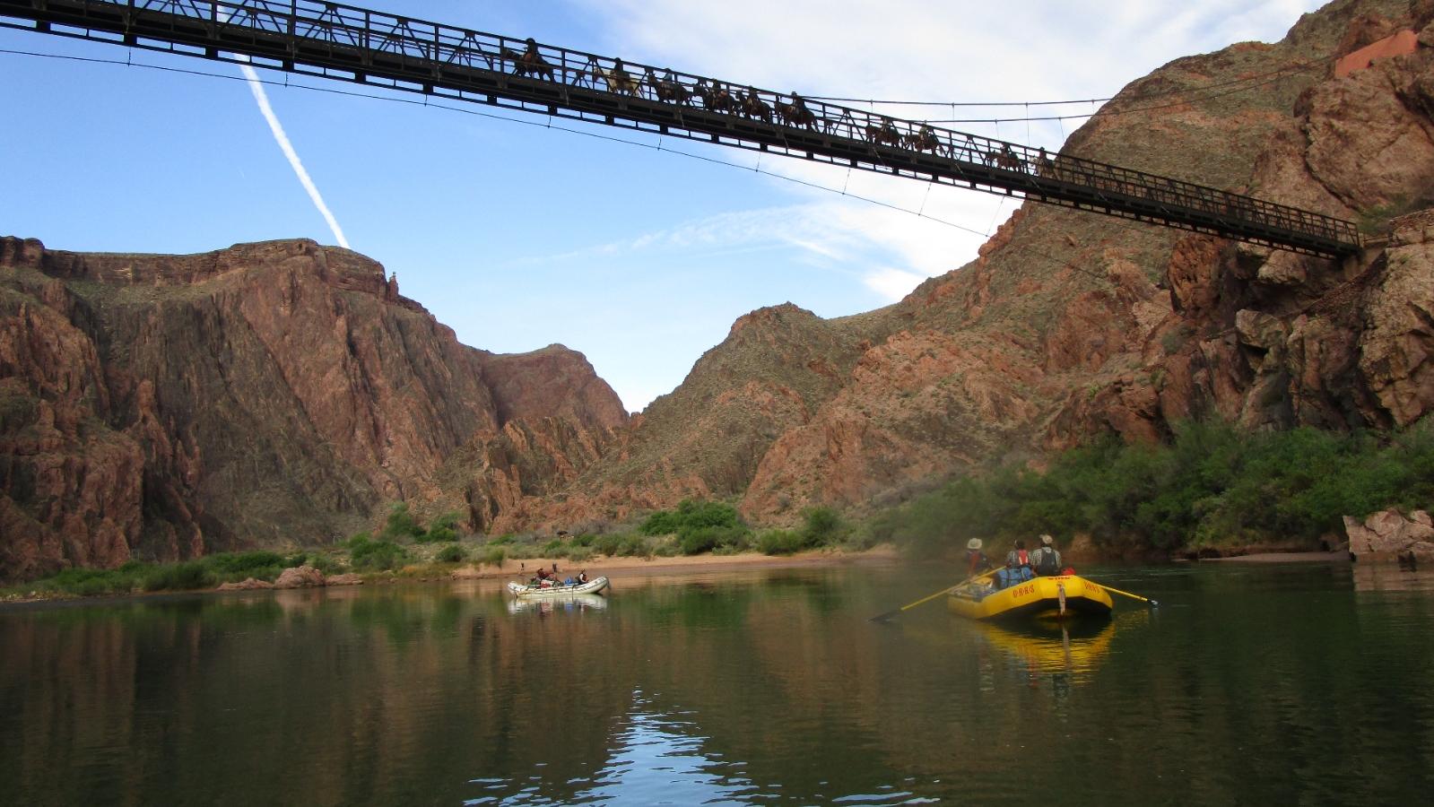 people rafting on a river and riding horseback across a bridge