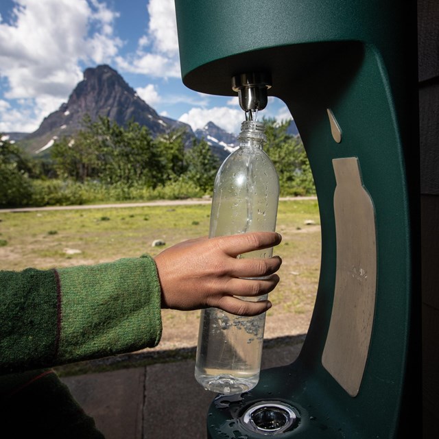 person refills water bottle at a bottling station with mountain in the background