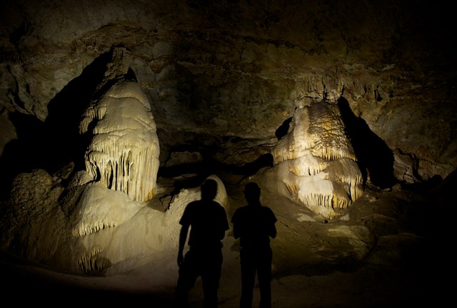 Visitors silhouetted in flashlight beams, cave formations illuminated