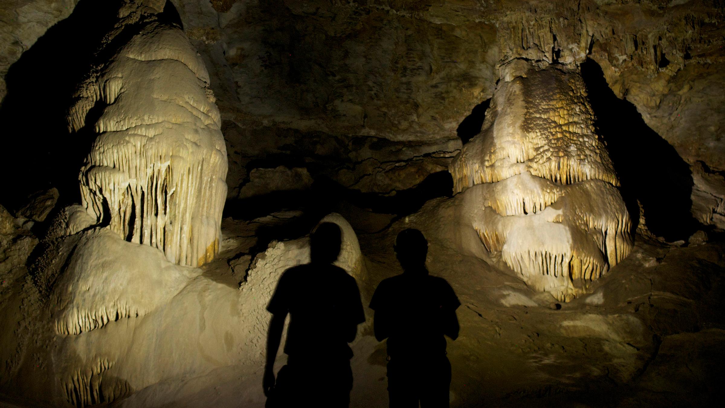 Visitors silhouetted in flashlight beams, cave formations illuminated