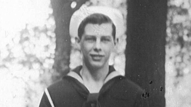 Black and white image of a sailor in a dark blue uniform and white sailor hat