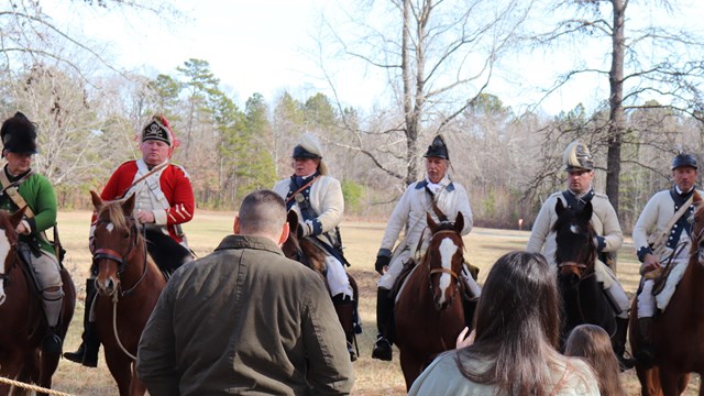 Several reenactors in white military uniforms on horseback. 