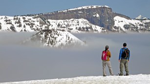 Two snowshoers gaze at the lake, filled with fog.