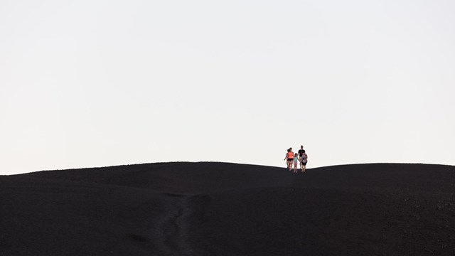 A family hikes down the bare cinder slope of Inferno Cone