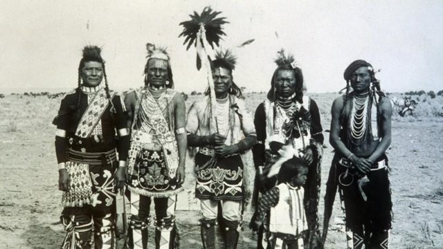 black and white photo of a group of five Shoshone dancers in traditional dress