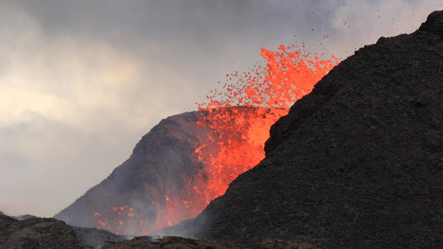 orange lava erupting from the side of a black cone