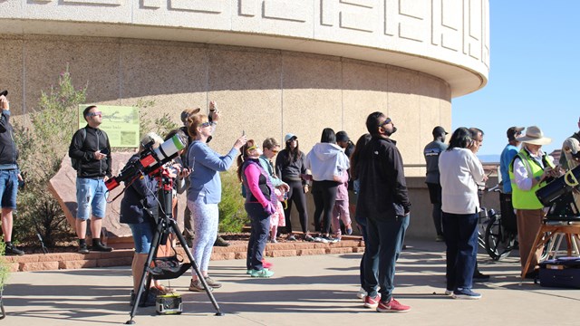 People outside a visitor center watching a solar eclipse wearing eclipse glasses
