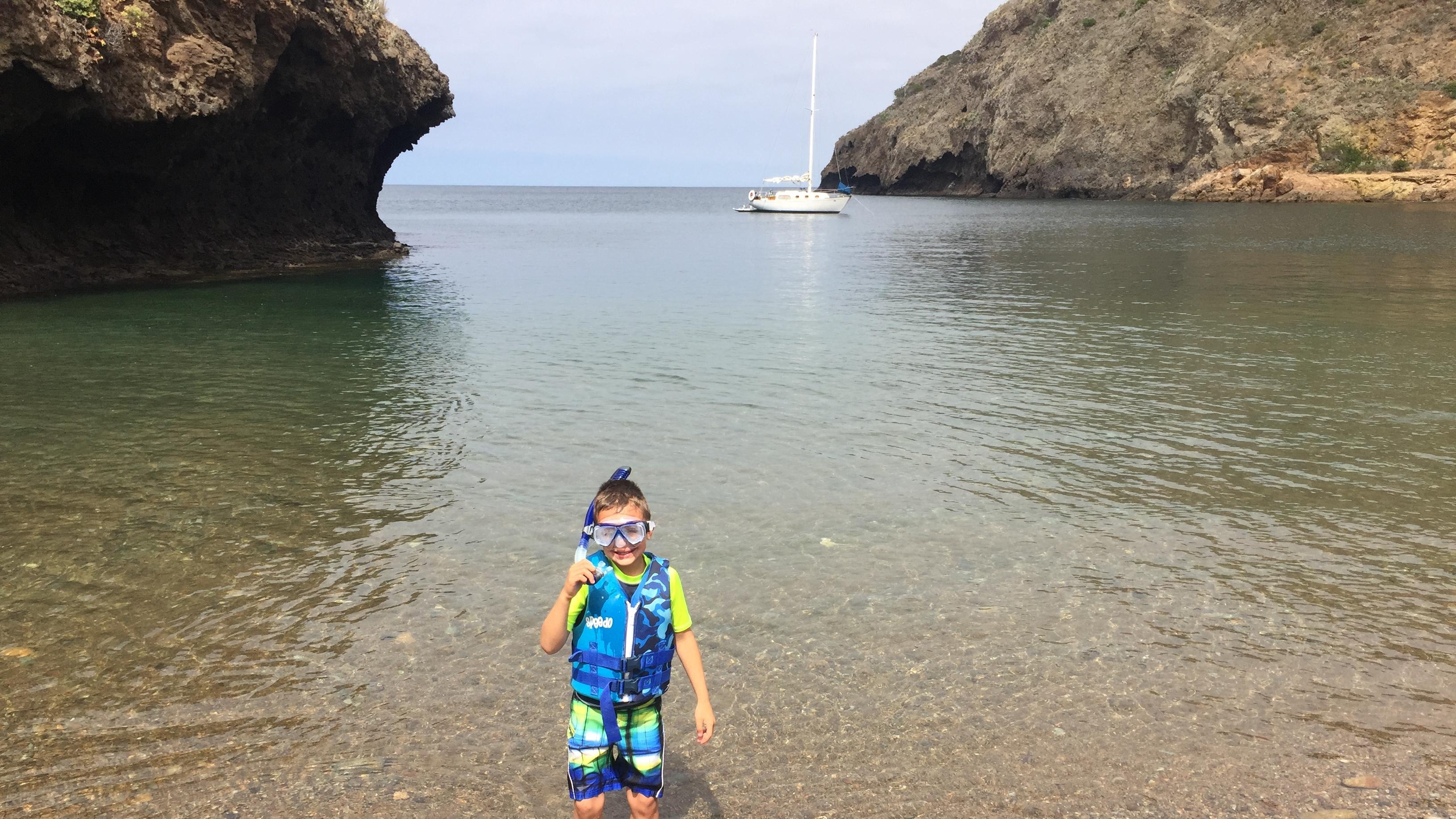 Kid in snorkel gear staking in a cove