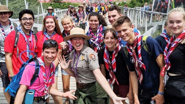 A park ranger in a funny pose with scouts wearing neckerchiefs all around her