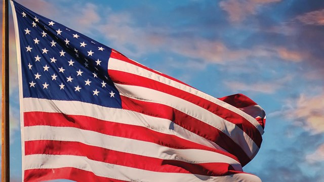 American flag flying on a pole with blue skies and clouds. 