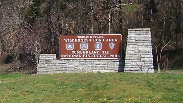 Brown sign along road with a mountain in the background. The sign reads Wilderness Road Area.