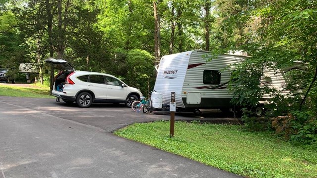 camper in the woods with a car and bike next to it