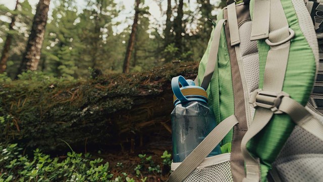 Backpack with a water bottle sitting on ground in the forest.