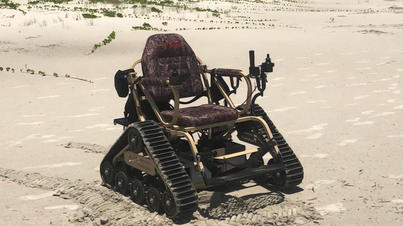 Cartoon drawing of an electric wheelchair with treads instead of wheels words "All Terrain Georgia"