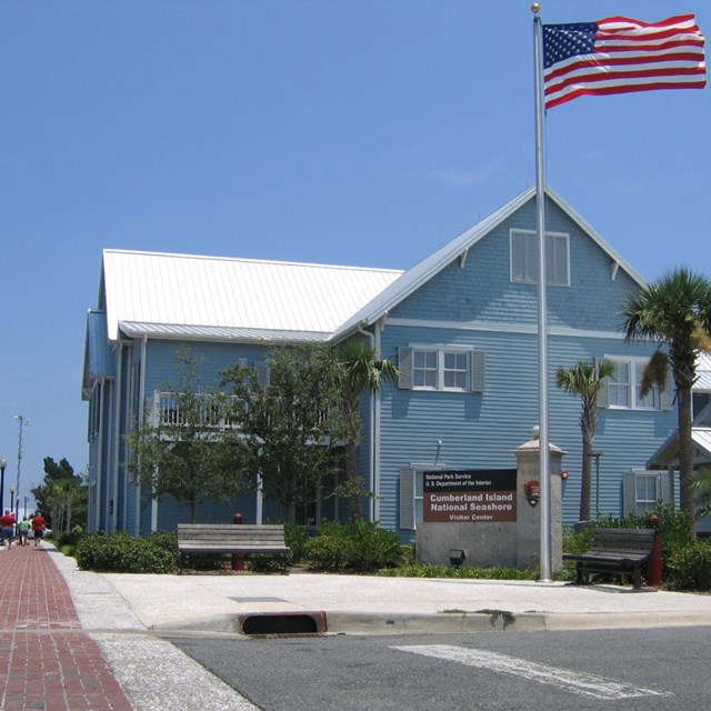 Two story blue building along brick sidewalk. Sign reads 