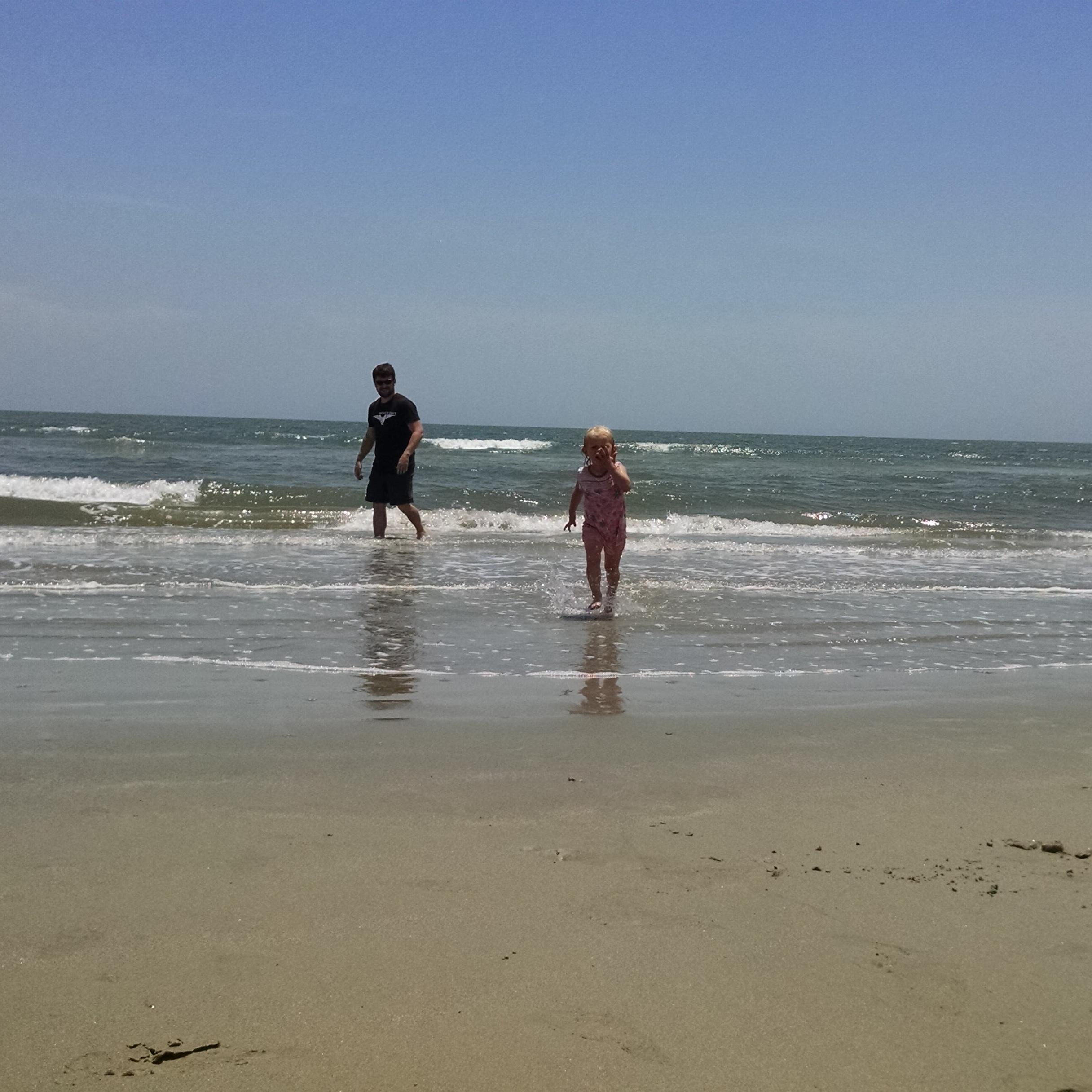 Man and young girl play in the surf on the beach