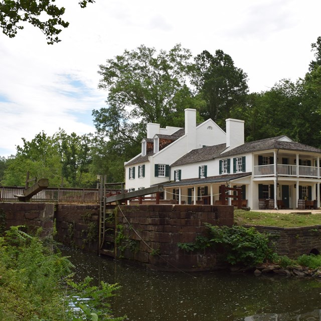 A large, two story structure with porches and chimneys beside a canal lock. 