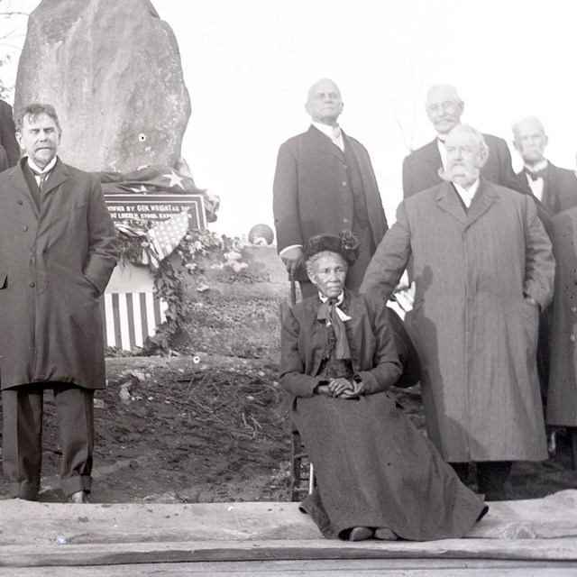 Elizabeth Thomas, seated, with Civil War Veterans beside a stone monument at Fort Stevens, 1911