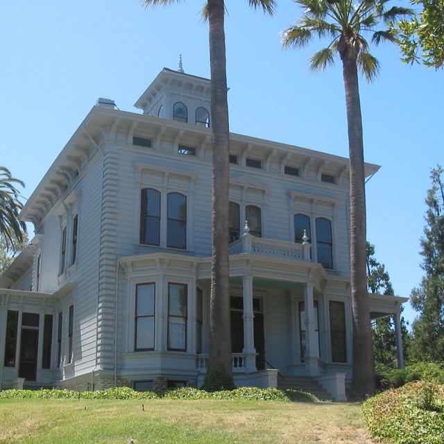 A rectilinear two-story house in a sunny location, beside palm trees, John Muir NHS.