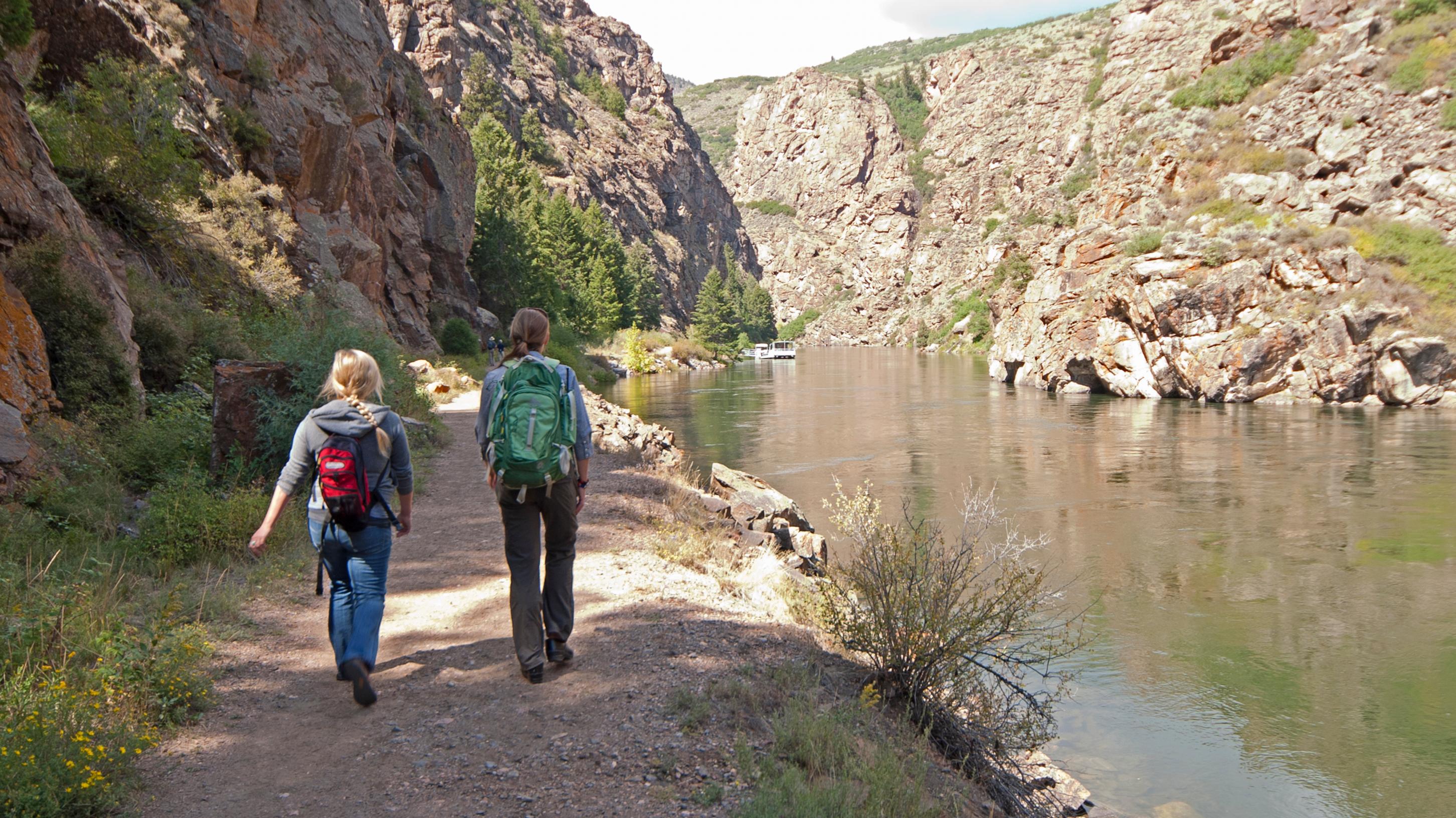 A photo of two people hiking on a path along a waterway