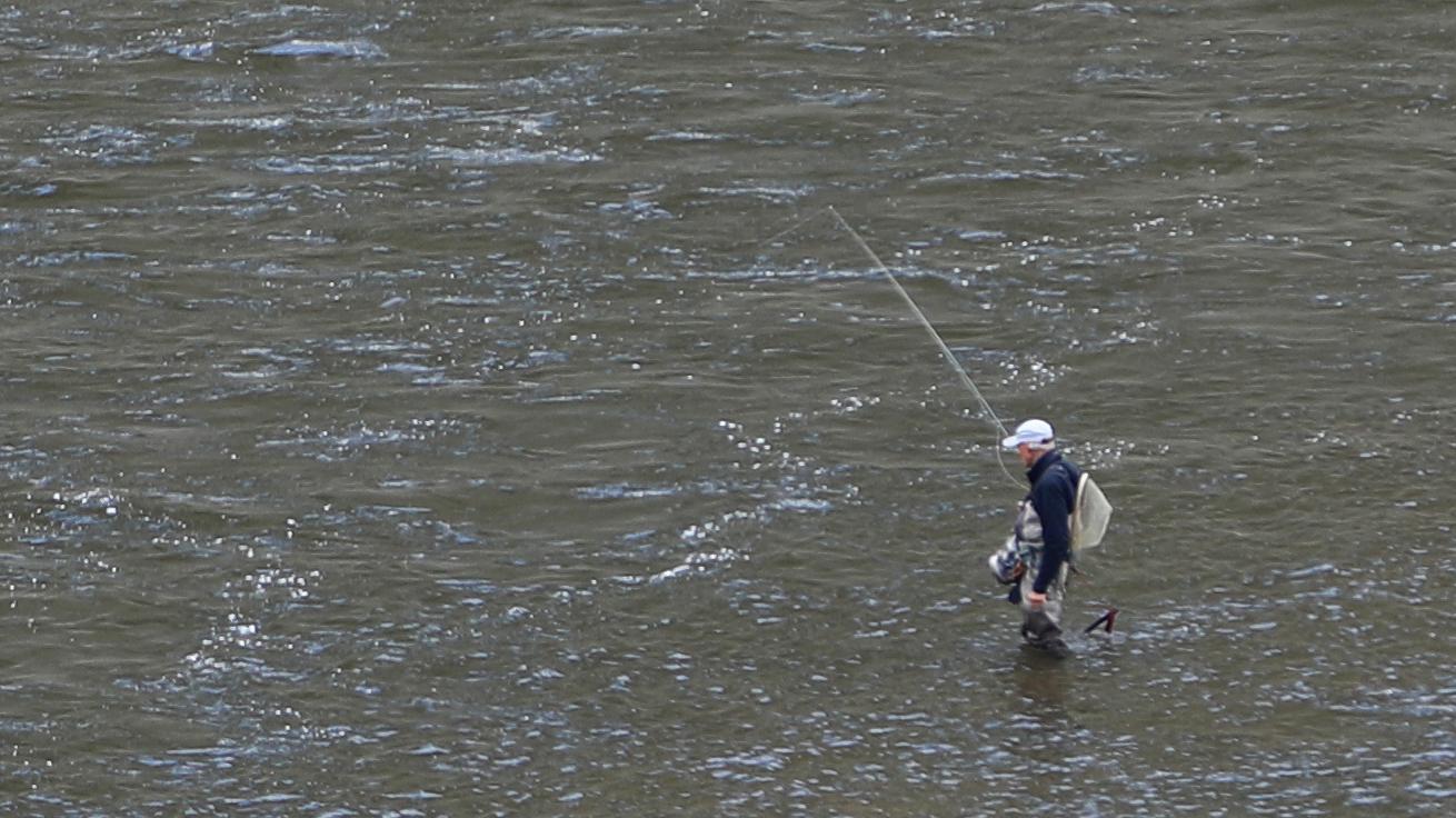 A person with a fishing rod and gear wades out into a river