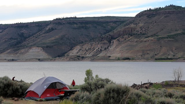 A small red tent in a grassy area. Mesas and water are in the background.