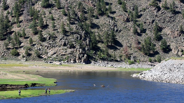 People fishing in a river surrounded by dark, steep canyon walls