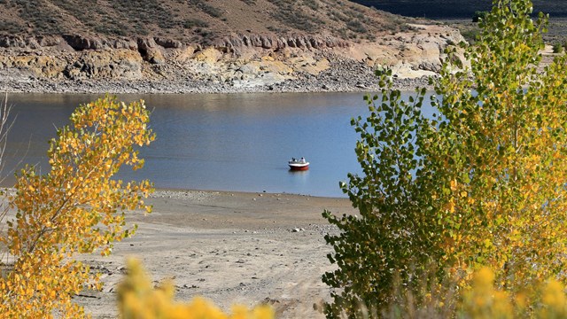 A small white and red boat floats on blue water. Yellow trees are in the foreground.