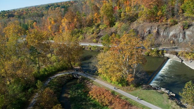 Aerial view of a green-brown river at the Canal Diversion Dam; colorful fall trees line the banks.
