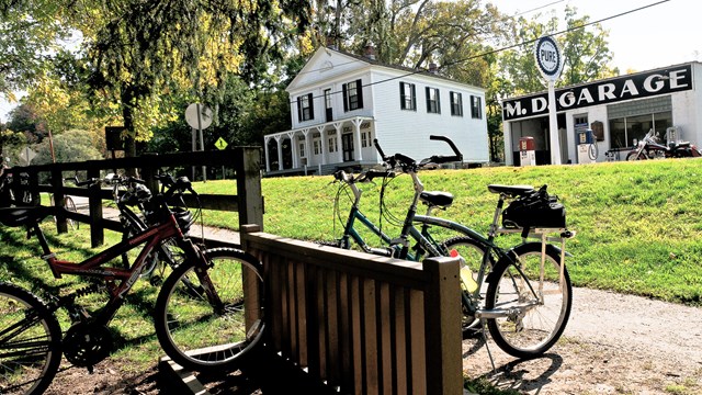 Bikes at a bike rack; across the street, two white buildings, one with painted sign, "M.D. Garage".