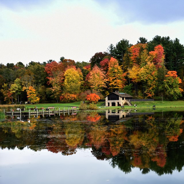 Stone shelter in the distance across a body of water, colorful trees up on the hillside behind it.