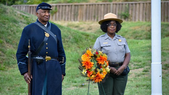 a reenactor and park ranger stand behind a wreath