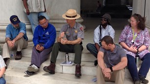Park ranger chats with people while sitting on steps.